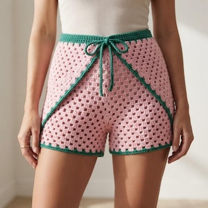 May include: Crochet shorts featuring a pink granny square pattern with a solid green waistband and trim. The shorts include a matching green drawstring tie at the center front, creating a distinct layered look with the green border detailing.