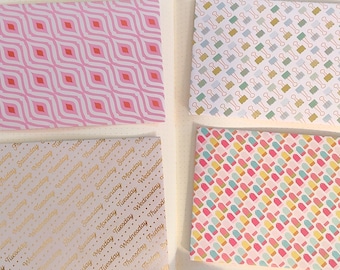 May include: Four patterned papers with different designs. One has a pink and white geometric pattern, another has a pattern of binder clips, a third has the days of the week in gold, and the last has a popsicle pattern.