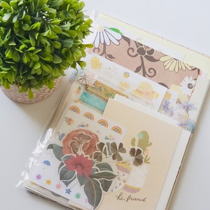 May include: A set of colorful paper ephemera, including patterned paper, stickers, and washi tape. The set features a floral theme with butterflies, clovers, and a cactus. The text "hi, friend." is visible on one of the papers.