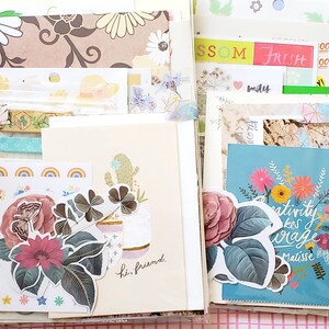 May include: A collection of colorful paper ephemera, including patterned paper, stickers, and cards. The cards feature floral designs and inspirational quotes, such as "Creativity takes courage." and "Hi, friend."