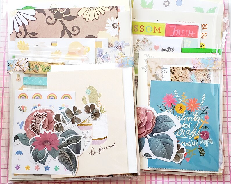 May include: A collection of colorful paper ephemera, including patterned paper, stickers, and cards. The cards feature floral designs and inspirational quotes, such as "Creativity takes courage." and "Hi, friend."