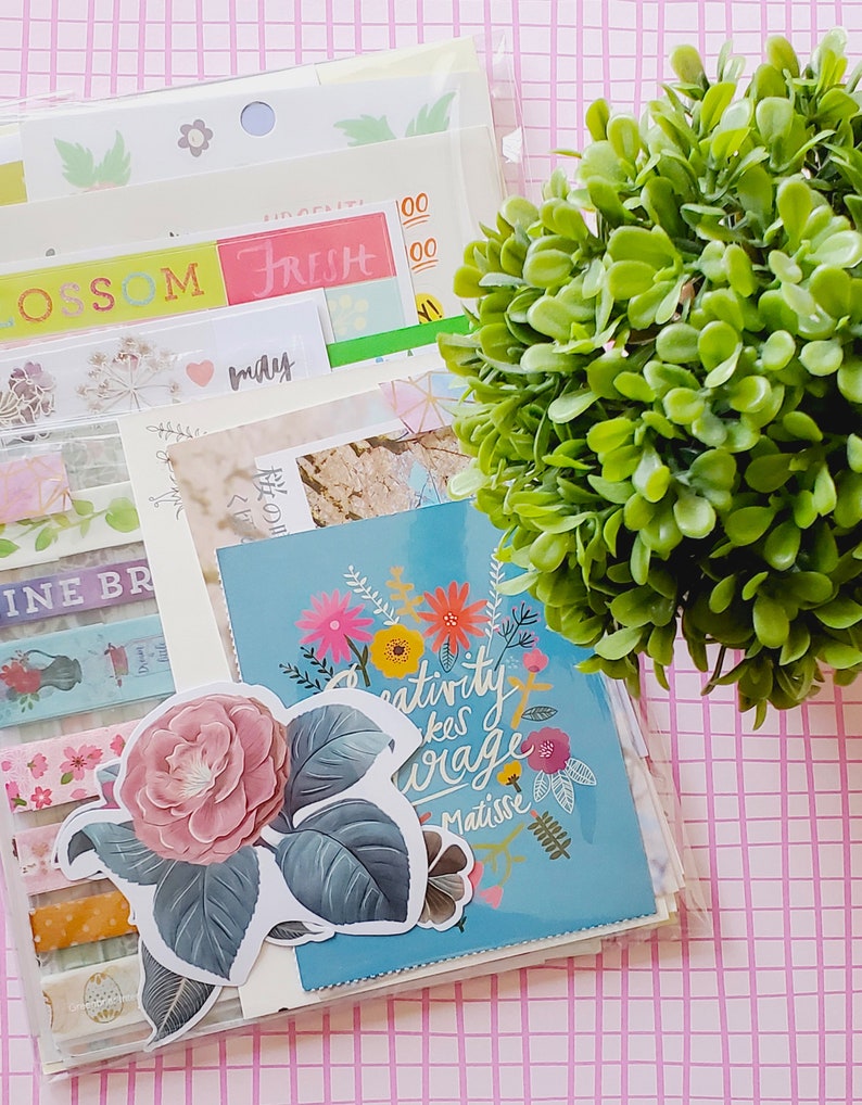 May include: A clear plastic envelope filled with colorful paper, stickers, and washi tape. The envelope is decorated with a floral design and the text "Creativity takes courage Matisse".