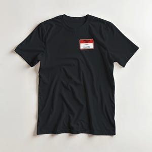 Puede incluir: Camiseta negra con una etiqueta roja y blanca que dice "HELLO I'M STILL DEALING". La camiseta es de estilo cuello redondo clásico, perfecta para uso casual. La etiqueta es rectangular con esquinas redondeadas.
