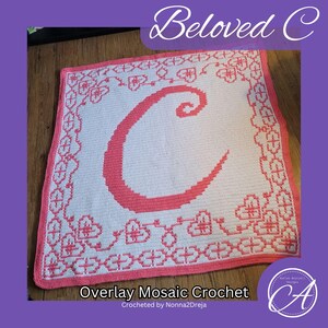 May include: A pink and white crochet blanket with a large pink letter "C" in the center. The blanket has a border of pink flowers and leaves. The text "Overlay Mosaic Crochet" and "Crocheted by Nonna2Dreja" is at the bottom of the blanket.