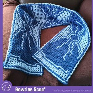May include: A crochet scarf featuring a two-tone blue and light blue geometric pattern of interlocking bowties. The scarf displays a repeating design with sharp, angular lines and a textured stitch throughout the entire length of the fabric.