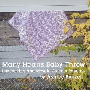 May include: A purple and white crocheted baby blanket with a heart pattern. The blanket is draped over a wooden fence with a chain link fence in the background. The text "Many Hearts Baby Throw Interlocking and Mosaic Crochet Patterns by Ashlee Broizell" is printed below the blanket.