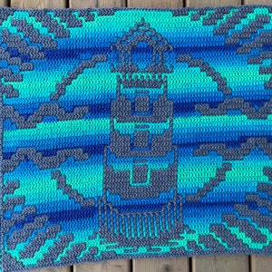 May include: A crocheted blanket with a geometric pattern in shades of blue and green. The blanket is made with a textured yarn and has a fringe border.