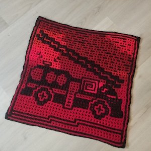 Peut inclure: Un plaid carré crocheté rouge et noir avec un motif de camion de pompiers pixélisé.