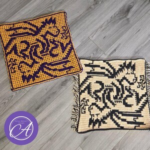 May include: Two crocheted squares with geometric patterns. The first square is yellow with a purple design. The second square is beige with a black design. Both squares have fringe around the edges.