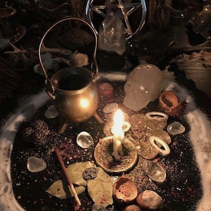 May include: A mystical scene featuring a small brass cauldron, a lit candle, and a pentagram. Clear quartz crystals, dried herbs, and other ritualistic items are arranged on a dark surface, creating a spiritual ambiance. The image has a warm, inviting tone.