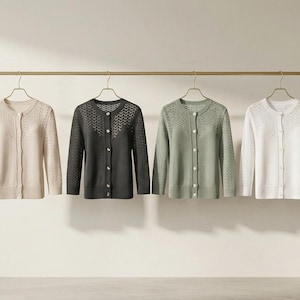 May include: Four cardigans in cream, charcoal, sage green, and white hang from a gold bar. Each has a round neckline, long sleeves, and an openwork design on the upper chest. The sweaters are buttoned up. The image is well-lit.