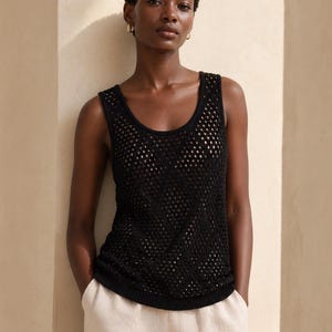 Pode incluir: Um top preto de malha aberta com decote redondo. O top &eacute; usado com cal&ccedil;as de cor clara. A modelo usa brincos de argola dourados. O fundo &eacute; de cor bege neutra.
