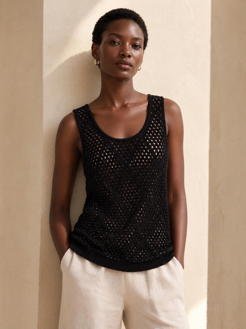 Pode incluir: Um top preto de malha aberta com decote redondo. O top &eacute; usado com cal&ccedil;as de cor clara. A modelo usa brincos de argola dourados. O fundo &eacute; de cor bege neutra.
