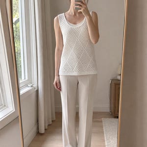 Puede incluir: Un top blanco sin mangas con una superposici&oacute;n de punto con estampado de diamantes, combinado con pantalones de pierna ancha de color beige claro. El conjunto incluye una camiseta interior con cuello redondo y zapatos beige a juego. El conjunto se captura en un espejo de cuerpo entero.
