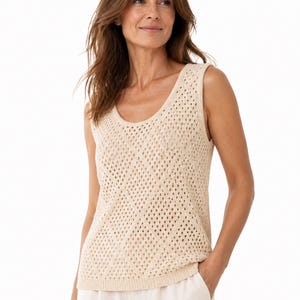 May include: A cream-coloured sleeveless knit top with a scoop neckline and openwork design. The top is made of a soft, textured material and has a relaxed fit. The model is wearing the top with cream-coloured trousers.