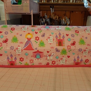May include: A pink fabric cover featuring a princess theme. The cover is decorated with castles, princesses, frogs, butterflies, and the text "Once Upon a Time." The cover has a pink border.