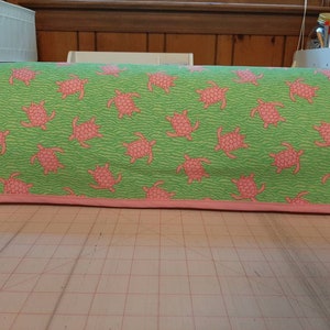 May include: A green and pink fabric sewing machine cover with a pattern of pink sea turtles on a green wave background.