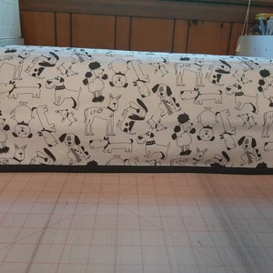 May include: A white sewing machine cover with a black and white dog pattern. The cover has a black trim around the edges.