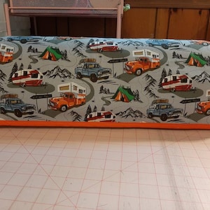 May include: A gray and orange fabric cover with a camping theme. The cover features a repeating pattern of vintage trucks pulling campers, mountains, and green tents.