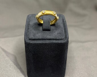 May include: A gold ring featuring a textured, ribbed band with a matte finish. The ring is accented with small, evenly spaced circular settings, each containing a single clear, sparkling stone embedded along the outer surface of the band.