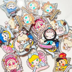 Pode incluir: Uma coleção de pins coloridos em estilo cartoon com vários personagens com penteados e roupas únicos. Muitos pins incluem o texto "15th Anniversary" em uma faixa. Os pins têm um acabamento brilhante e estão em um fundo branco.