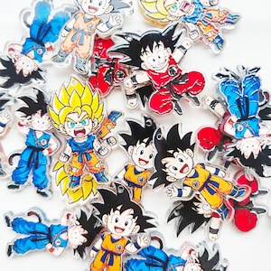 Puede incluir: Una colección de coloridos colgantes de acrílico con varios personajes en poses dinámicas. Los colgantes muestran personajes con pelo puntiagudo, vistiendo trajes en tonos azules, naranjas, rojos y amarillos. Los colgantes están sobre un fondo blanco.