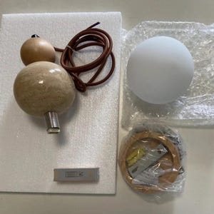 May include: A disassembled pendant light fixture with a spherical frosted glass shade, a wooden base, and a decorative element with two wooden spheres and a textured stone sphere. The fixture includes a brown cord and a small rectangular component.