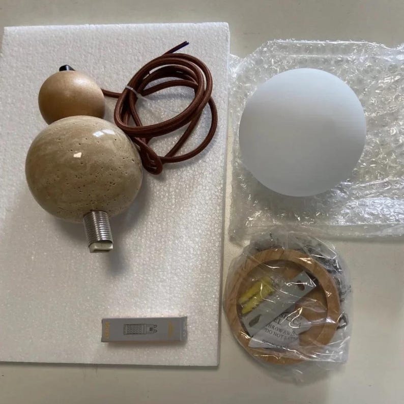 May include: A disassembled pendant light fixture with a spherical frosted glass shade, a wooden base, and a decorative element with two wooden spheres and a textured stone sphere. The fixture includes a brown cord and a small rectangular component.