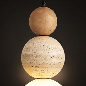 May include: A modern pendant light fixture featuring three stacked spheres. The top sphere is made of light-colored wood, the middle sphere has a textured, beige stone appearance, and the bottom sphere is a glowing white. The fixture hangs from a black metal rod.