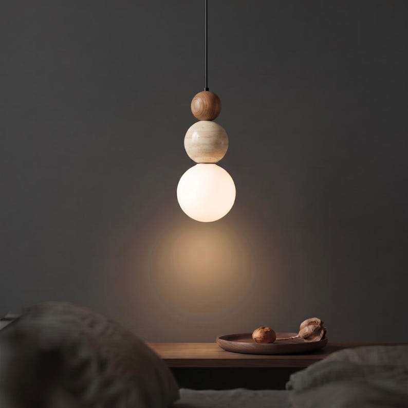 May include: A modern pendant light fixture with a stacked design. The fixture features a small, dark brown wooden sphere at the top, followed by a light-colored wooden sphere, and a large, glowing white glass sphere at the bottom. The light hangs from a black cord.