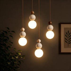 Op de afbeelding: Vier hanglampen met een modern design. Elke lamp heeft een gloeiende, bolvormige lamp die aan een dun snoer hangt. De snoeren zijn bevestigd aan decoratieve elementen van hout en steen, waardoor een gelaagd effect ontstaat. De lampen staan tegen een donkere achtergrond.