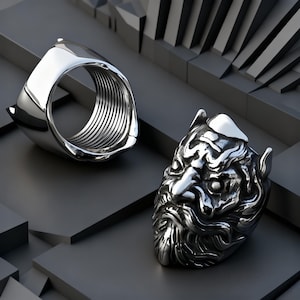 May include: A silver-toned ring featuring a detailed, sculpted face with a beard and prominent features on the front, paired with a separate, hollow, threaded metal component that has a smooth exterior and a ribbed interior surface.
