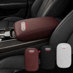 May include: A maroon car centre console armrest cover with a logo, shown installed on a vehicle console and as three separate oval-shaped covers in maroon, black, and white, each featuring a small logo on the upper portion of the surface.
