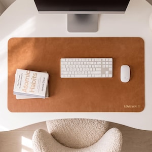 May include: A rectangular tan leather desk mat with rounded corners, featuring the embossed text "LOVE YOU" and a small heart symbol in the bottom right corner. A white computer keyboard and a white computer mouse are placed on the mat.