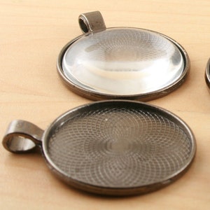 May include: Two round, silver-toned metal pendant trays with a decorative pattern. One tray has a clear glass insert, while the other has a solid metal insert.