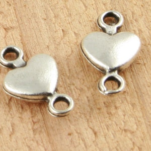 May include: Two silver heart-shaped connector charms with two jump rings on each charm. The charms are smooth and shiny.