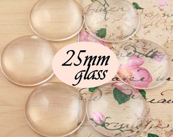 May include: A collection of clear, round glass cabochons, some with a pale peach hue, and others with a floral design. The text "25mm glass" is in the center. These glass pieces are suitable for crafting and jewelry making.