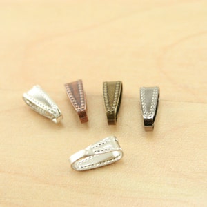 May include: Five silver, copper, and bronze pendant clasps with a decorative beaded edge. The clasps are in the shape of a triangle with a rounded top.