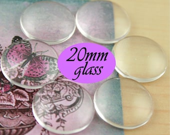 May include: A close-up of six clear glass cabochons, each measuring 20mm in diameter. The cabochons are arranged in a semi-circle on a pink and white patterned surface. The text "20mm glass" is printed in black on a purple background.