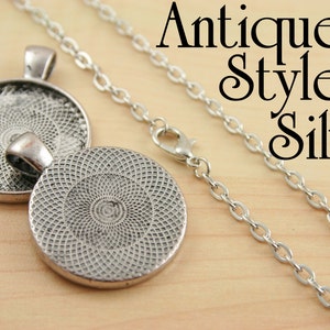 May include: A silver pendant necklace with a round, textured, silver charm. The charm has a circular design with a repeating pattern. The necklace has an antique style chain.