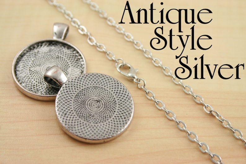 May include: A silver pendant necklace with a round, textured, silver charm. The charm has a circular design with a repeating pattern. The necklace has an antique style chain.