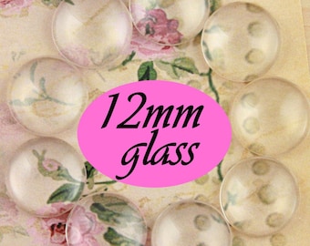 Può includere: Primo piano di otto cabochon di vetro trasparente, ognuno con un diametro di 12 mm. I cabochon sono disposti in cerchio su una superficie con motivo floreale. Il testo "12mm glass" è scritto in nero su un ovale rosa.