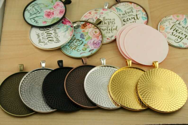 May include: Assortment of round metal trays with a decorative swirl pattern. The trays are in various finishes, including silver, gold, black, and copper. The trays are designed to hold round glass or plastic cabochons for jewelry making.