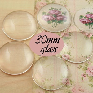 May include: Five clear glass cabochons, each measuring 30mm in diameter, are arranged on a floral patterned surface. The text "30mm glass" is printed on a pink background.