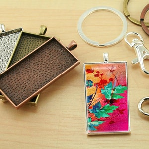 May include: A set of silver and bronze metal blank pendant trays with a colorful floral design in a silver frame. The trays are perfect for creating custom jewelry.