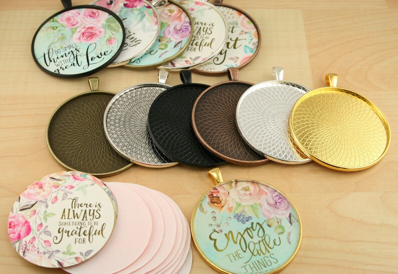 May include: Assortment of round metal pendant trays in gold, silver, bronze, and black. The trays have a decorative pattern and are ready to be filled with resin, images, or other embellishments.  The image also includes several blank round paper circles and finished pendants with floral designs and inspirational quotes.