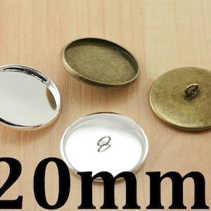 May include: Three silver and brass 20mm round metal blanks for crafting. The blanks have a smooth, shiny surface and a hole in the center.
