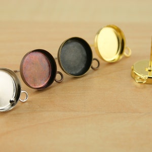 May include: Four round metal earring settings with a loop on the side. The settings are silver, copper, black, and gold.