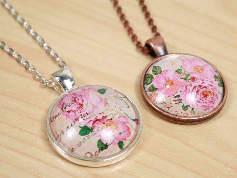 Pode incluir: Dois colares com pingentes redondos de vidro com rosas cor-de-rosa e um design floral vintage. Um colar tem uma corrente de prata e o outro uma corrente de cobre.