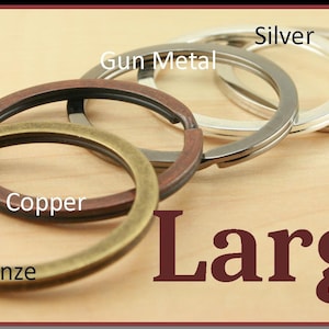 May include: Five large key rings in different metal finishes: bronze, dark copper, gun metal, silver, and platinum. The key rings are arranged in a row on a wooden surface. The word "Large" is printed in large, bold, maroon letters below the key rings.
